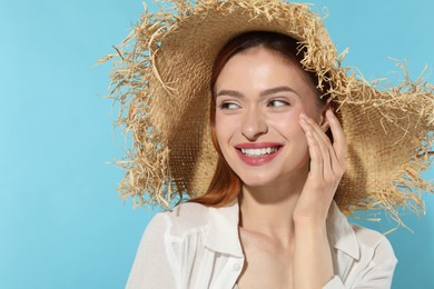 Beautiful young woman in straw hat on light blue background, space for text