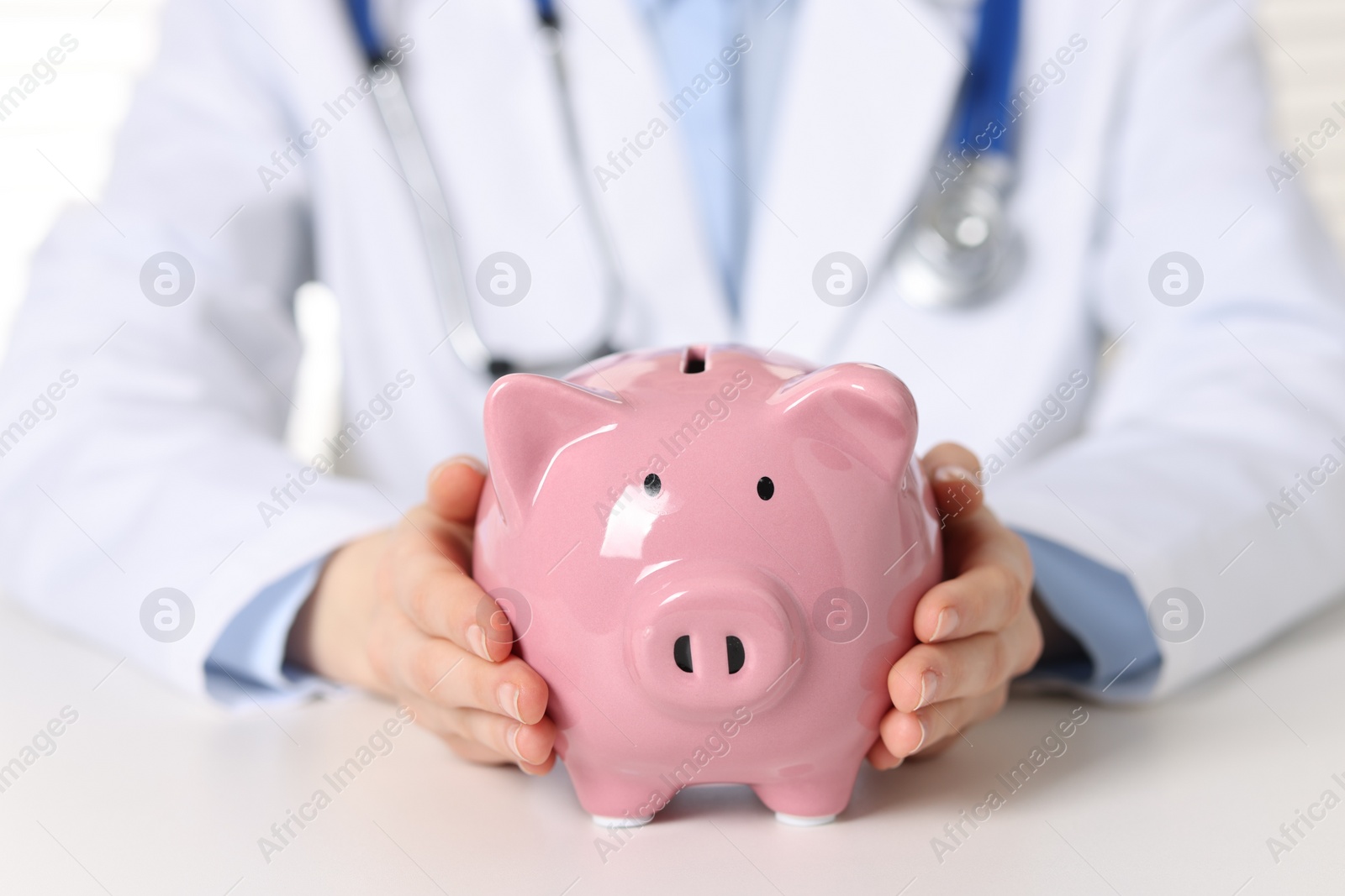 Photo of Doctor with piggy bank at white table, closeup