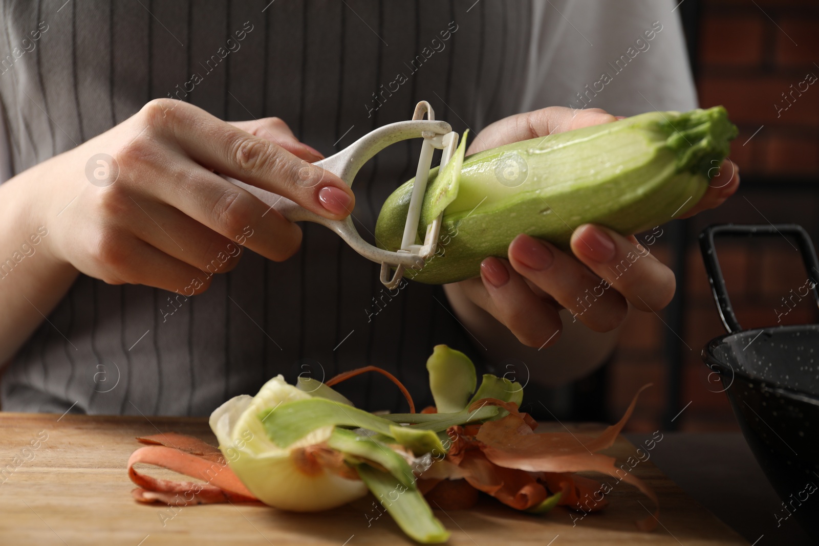 Photo of Woman peeling fresh zucchini at table indoors, closeup