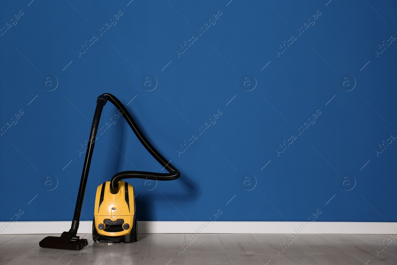 Photo of Modern yellow vacuum cleaner on floor near blue wall, space for text