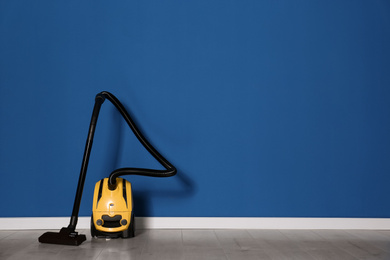 Photo of Modern yellow vacuum cleaner on floor near blue wall, space for text