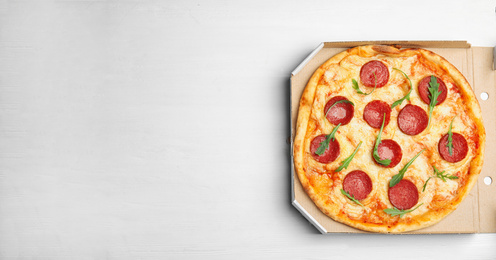 Photo of Tasty pepperoni pizza in cardboard box on white wooden table, top view. Space for text