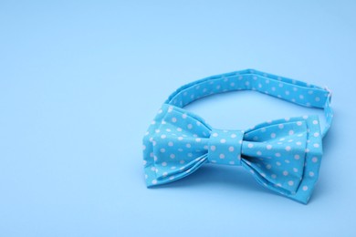 Stylish light blue bow tie with polka dot pattern on color background. Space for text