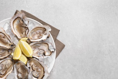 Photo of Delicious fresh oysters with lemon slices on light grey table, top view. Space for text