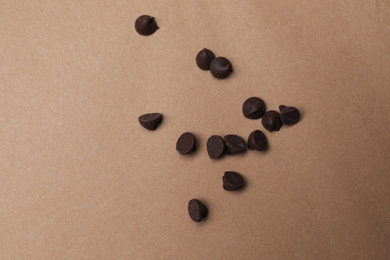 Delicious chocolate chips on brown background, top view