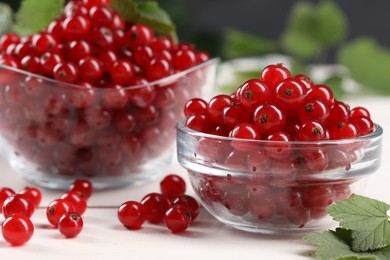 Photo of Many ripe red currants and leaves on white table, closeup