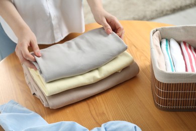 Woman folding clothes at wooden table indoors, closeup