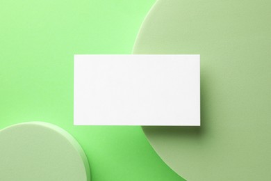 Empty business card and decorative elements on light green background, top view. Mockup for design
