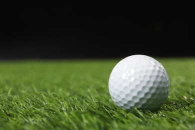 Golf ball on green grass against black background, space for text