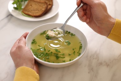 Photo of Man eating delicious chicken soup at light marble table, closeup