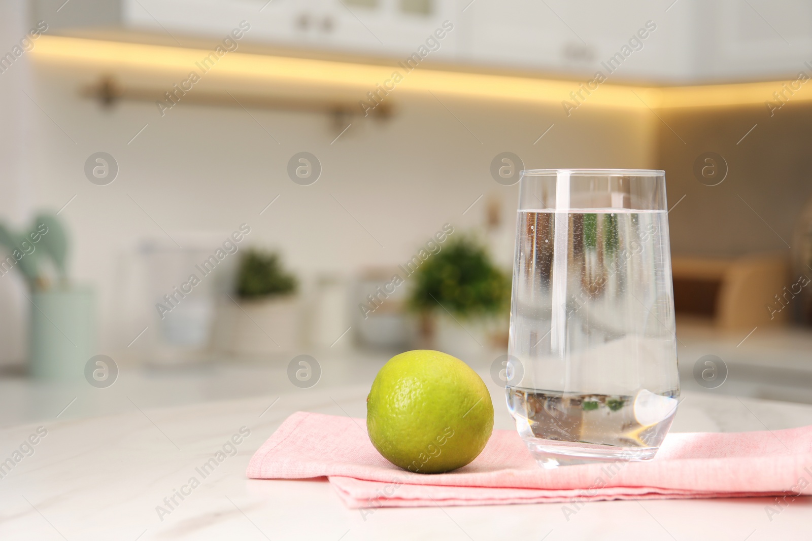 Photo of Filtered water in glass and lime on white marble table in kitchen, closeup. Space for text