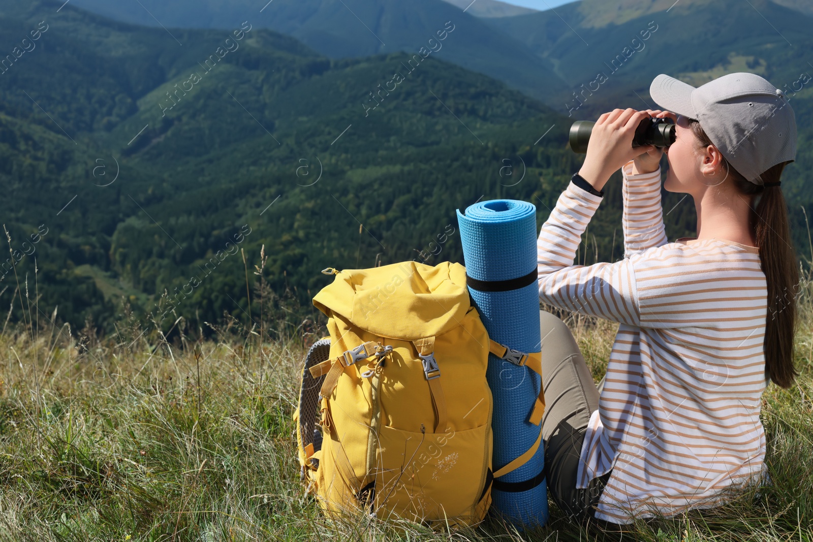 Photo of Tourist with hiking equipment looking through binoculars in mountains