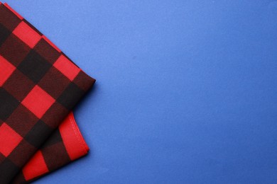 Folded red bandana with check pattern on blue background, top view. Space for text