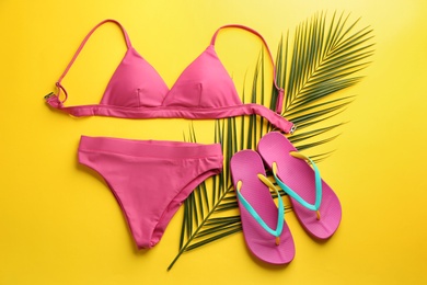 Photo of Beautiful pink bikini, flip flops and palm leaf on yellow background, flat lay