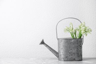 Beautiful lily of the valley bouquet in watering can on table near white wall, space for text