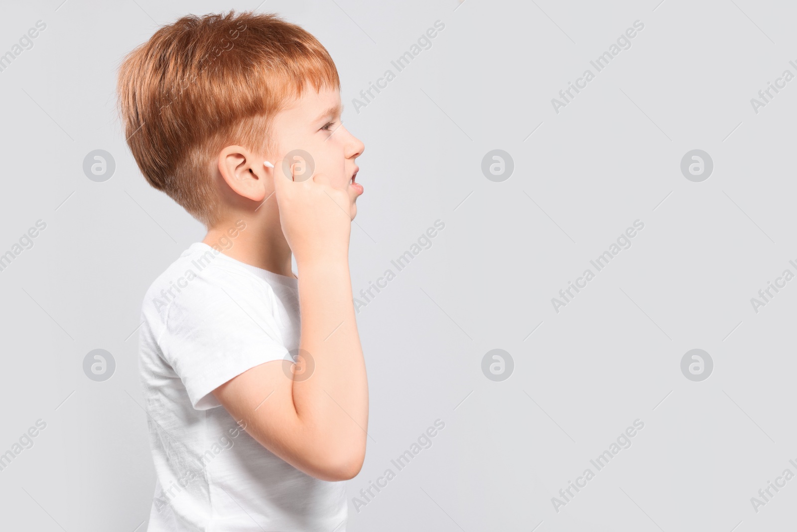 Photo of Little boy cleaning ear with cotton swab on light grey background. Space for text