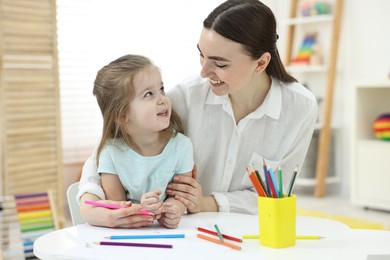 Photo of Mother and her little daughter drawing with colorful pencils at home