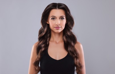 Gorgeous woman with shiny wavy hair on grey background. Professional hairstyling