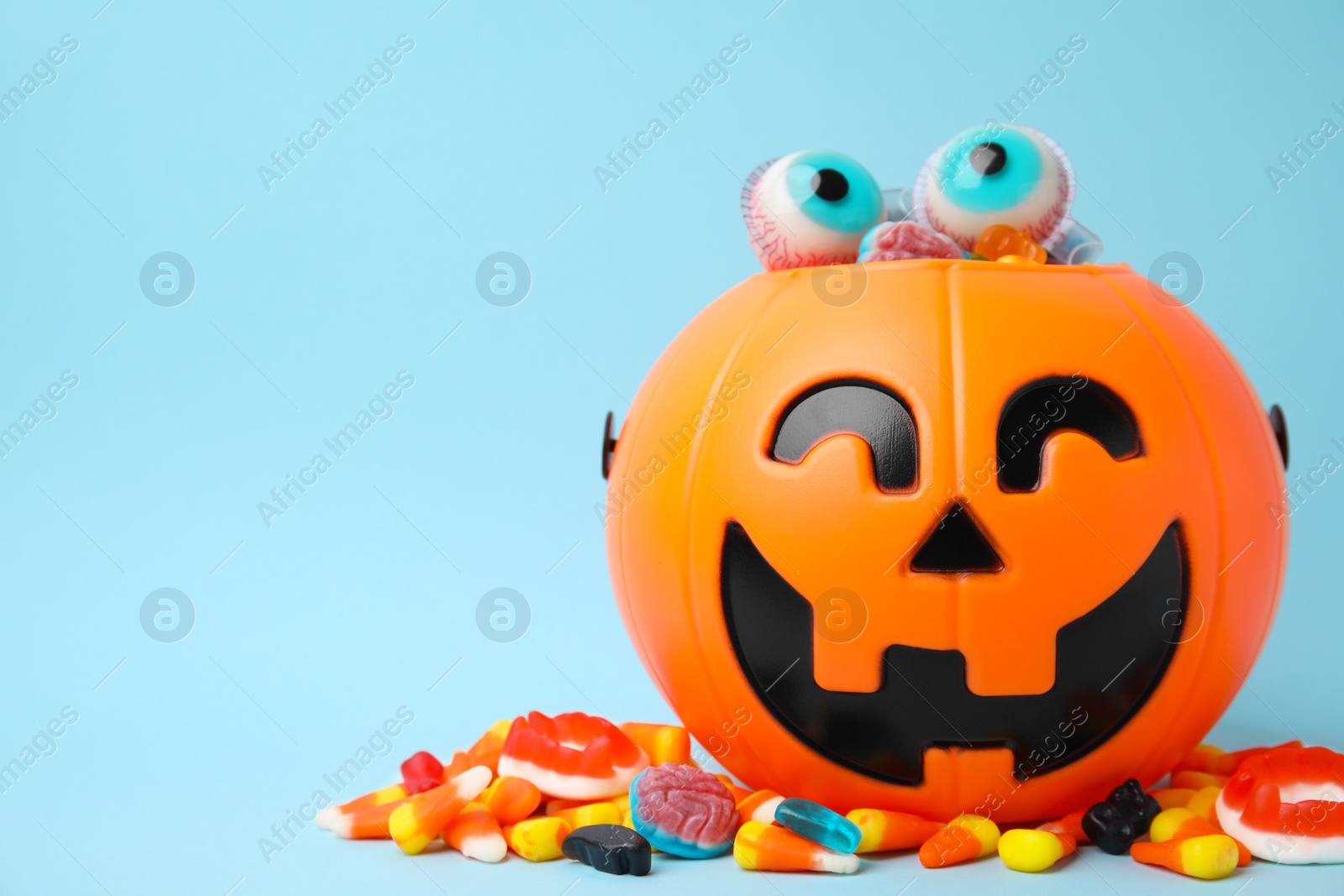 Photo of Halloween trick or treat bucket with different sweets on light blue, space for text