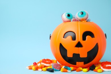 Photo of Halloween trick or treat bucket with different sweets on light blue, space for text