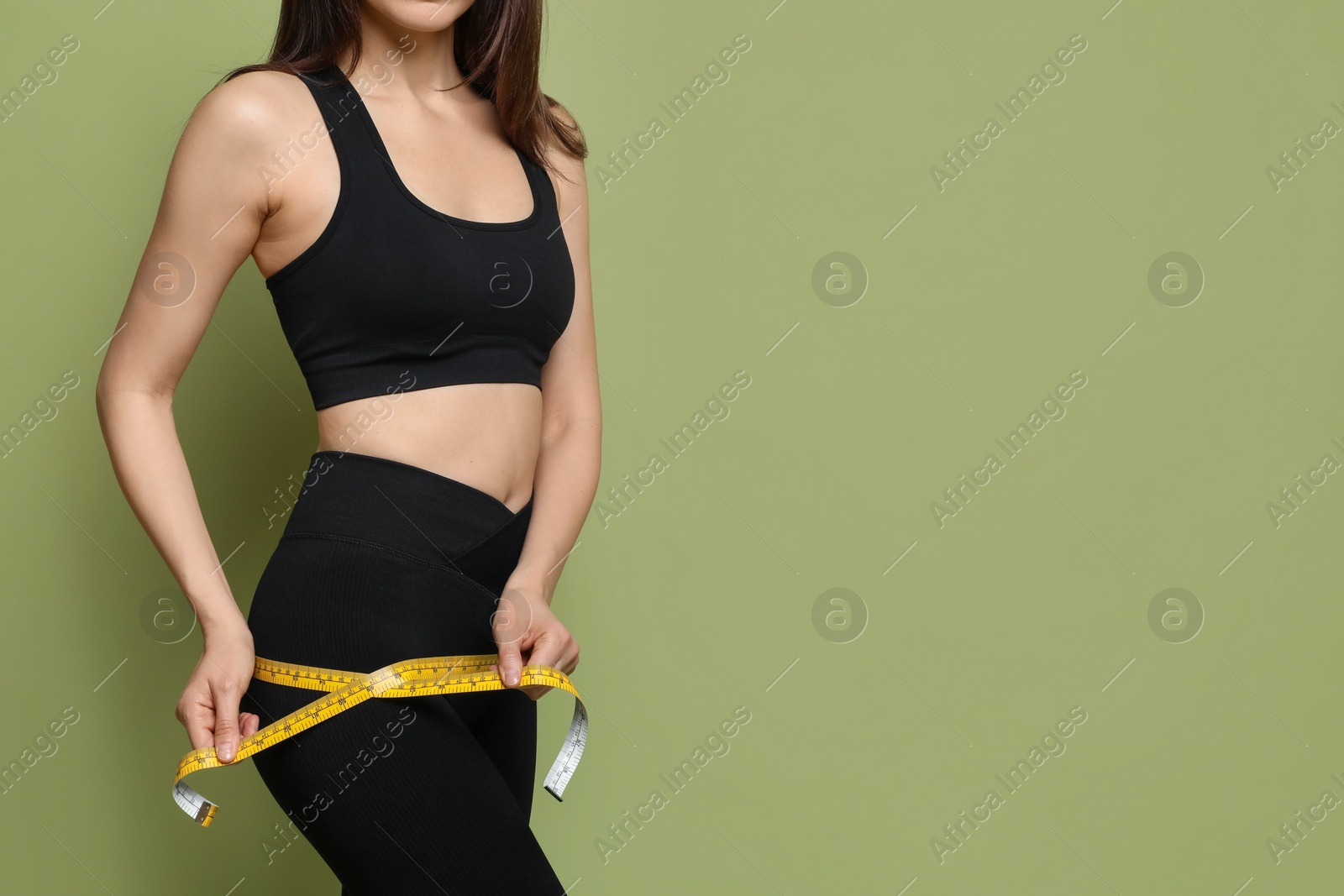 Photo of Woman with measuring tape showing her slim body on green background, closeup. Space for text