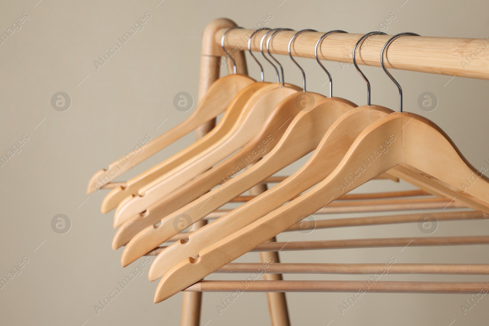 Photo of Clothes hangers on wooden rack against beige background, closeup