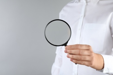 Woman holding magnifying glass on grey background, closeup. Find keywords concept