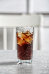 Glass of cold cola on table against blurred background. Space for text