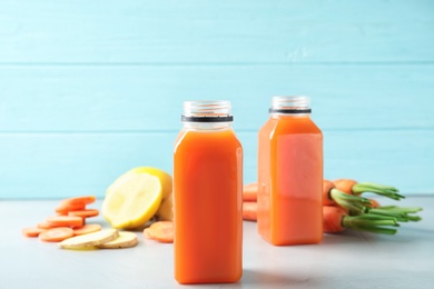 Photo of Bottles with carrot juice and fresh ingredients on table