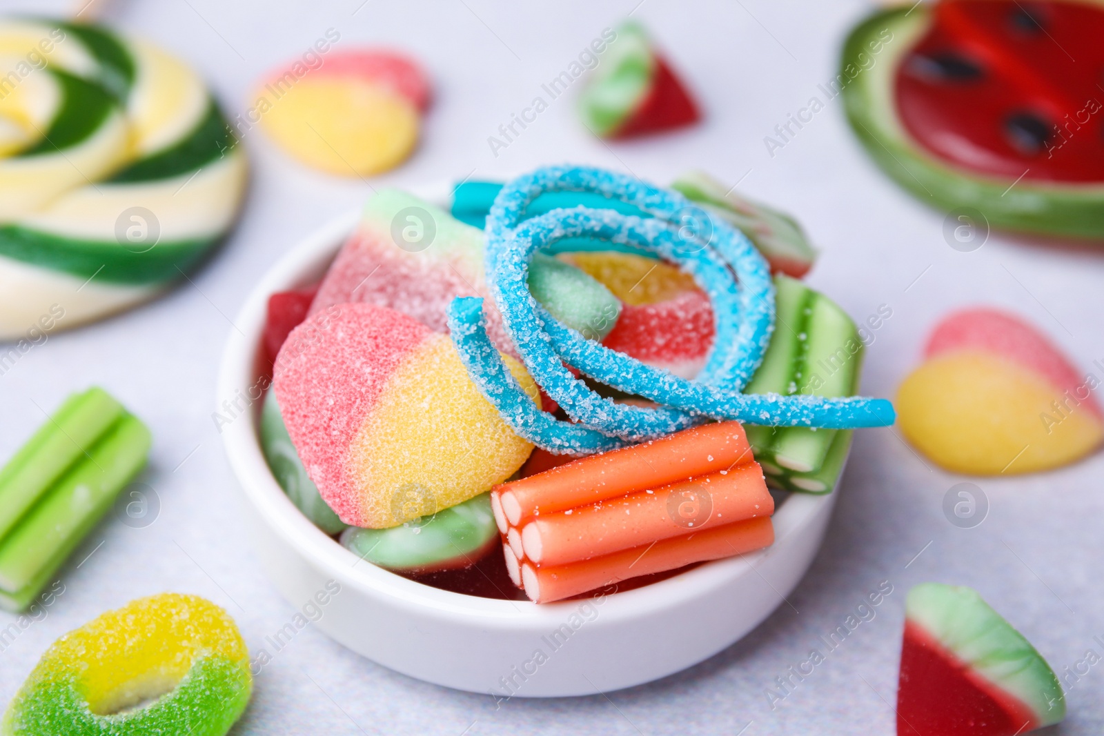 Photo of Bowl of tasty colorful jelly candies on white table, closeup