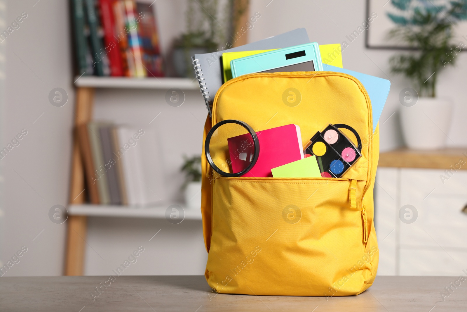 Photo of Yellow backpack with different school stationery on table indoors, space for text