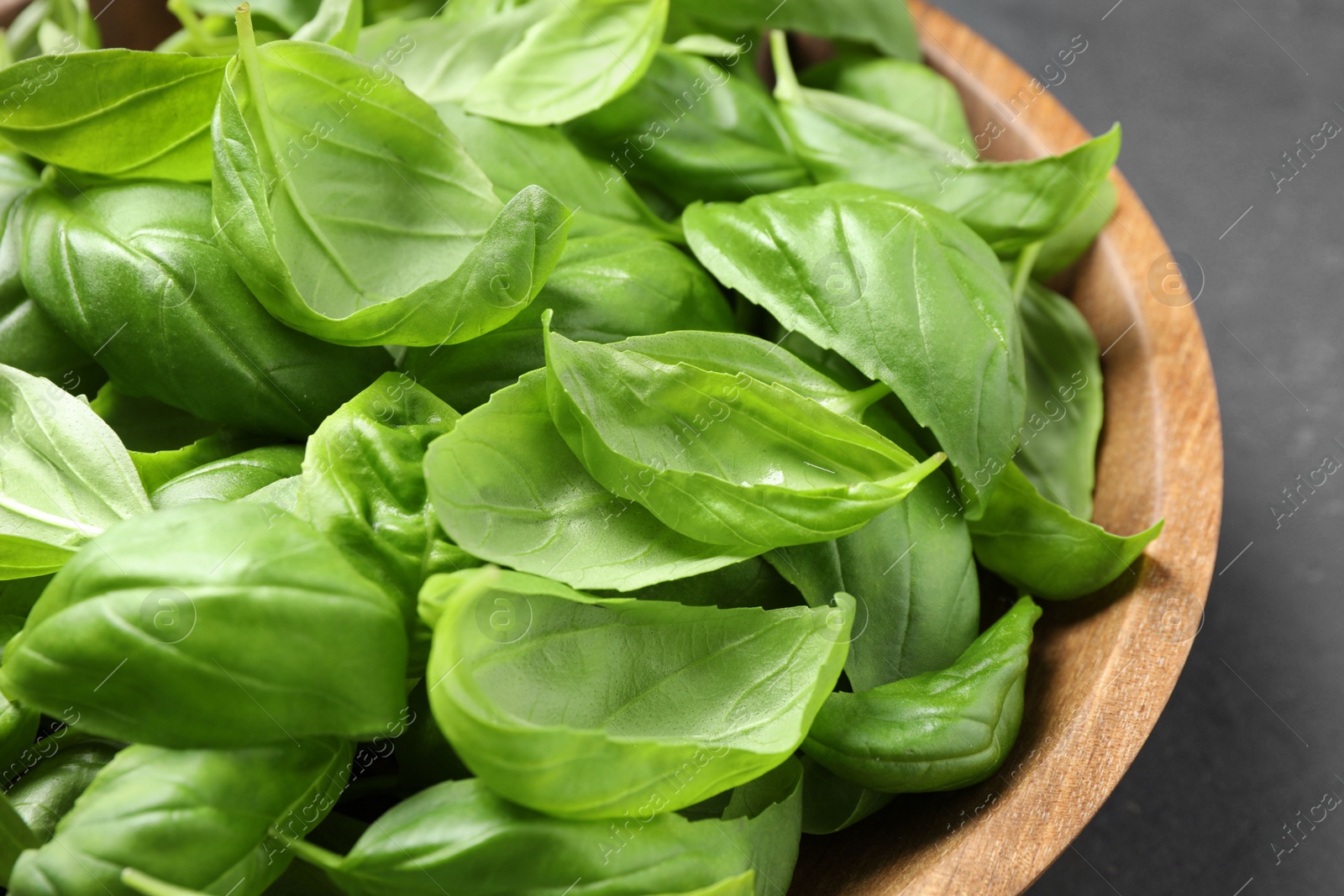 Photo of Fresh basil leaves in wooden bowl, closeup