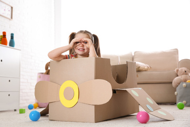 Cute little child playing with cardboard plane at home