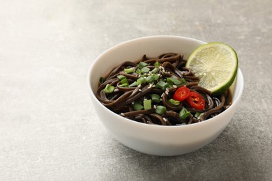 Photo of Tasty buckwheat noodles (soba) with sauce, onion and lime in bowl on light grey table. Space for text