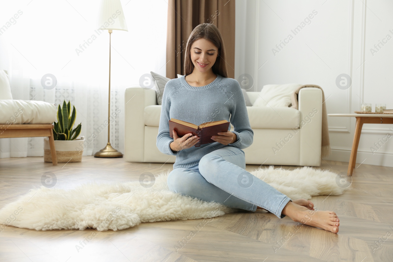 Photo of Beautiful young woman reading book at home. Floor heating concept