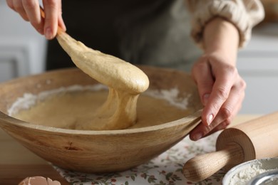Photo of Woman kneading dough with spoon in bowl at wooden table indoors, closeup