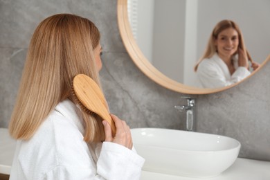 Photo of Beautiful woman brushing her hair near mirror in bathroom