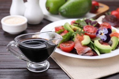 Photo of Tasty soy sauce and plate with salad on wooden table, selective focus
