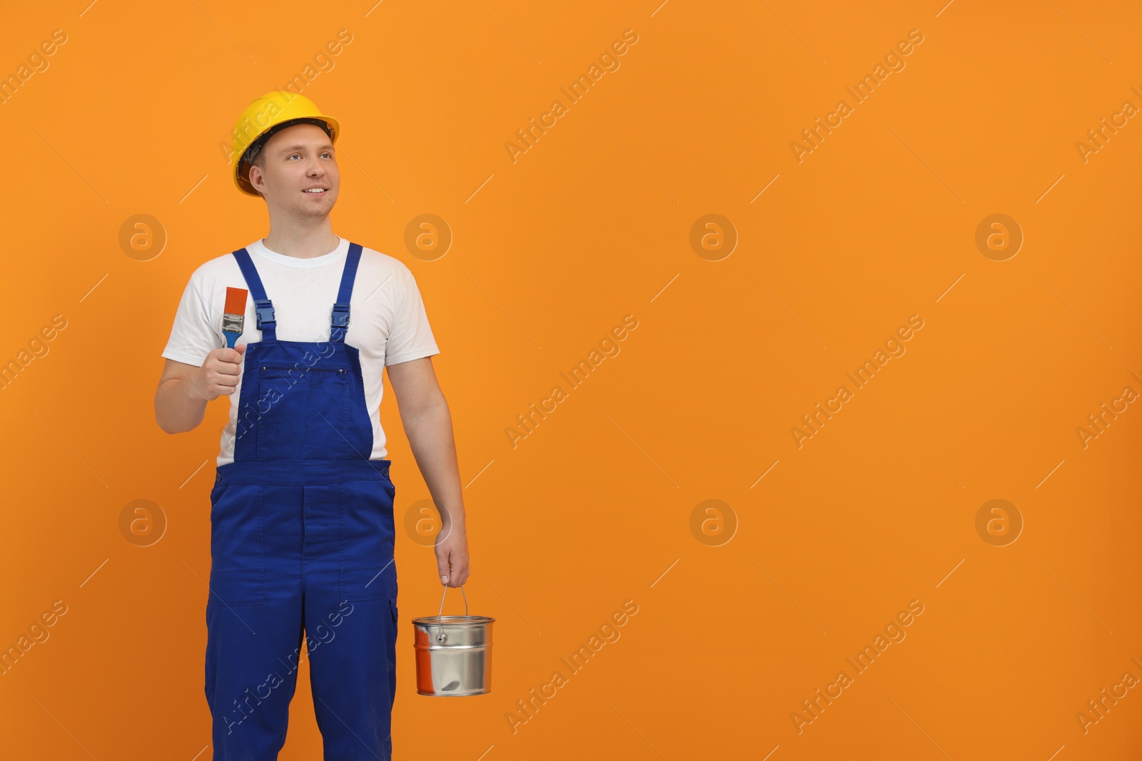 Photo of Worker holding paint brush and bucket near orange wall. Space for text