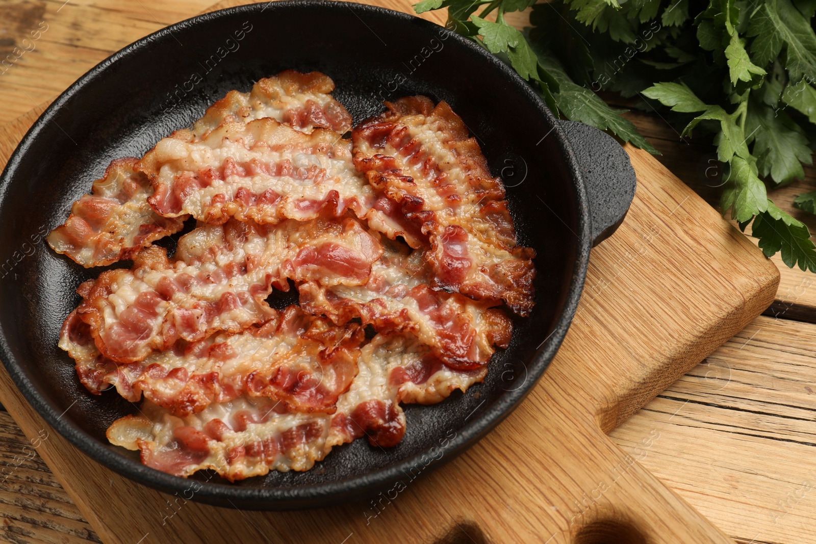 Photo of Delicious bacon slices in frying pan on wooden table, closeup