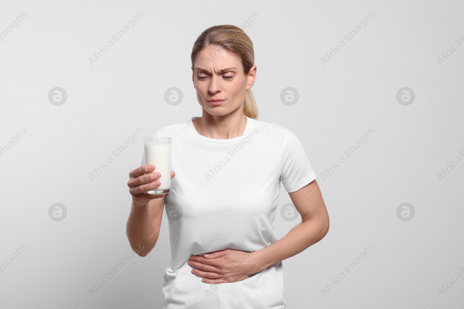 Photo of Woman with glass of milk suffering from lactose intolerance on white background