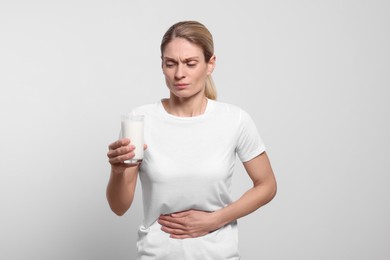 Woman with glass of milk suffering from lactose intolerance on white background