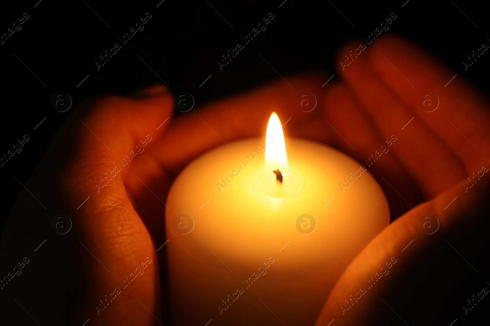 Photo of Woman holding burning candle in darkness, closeup