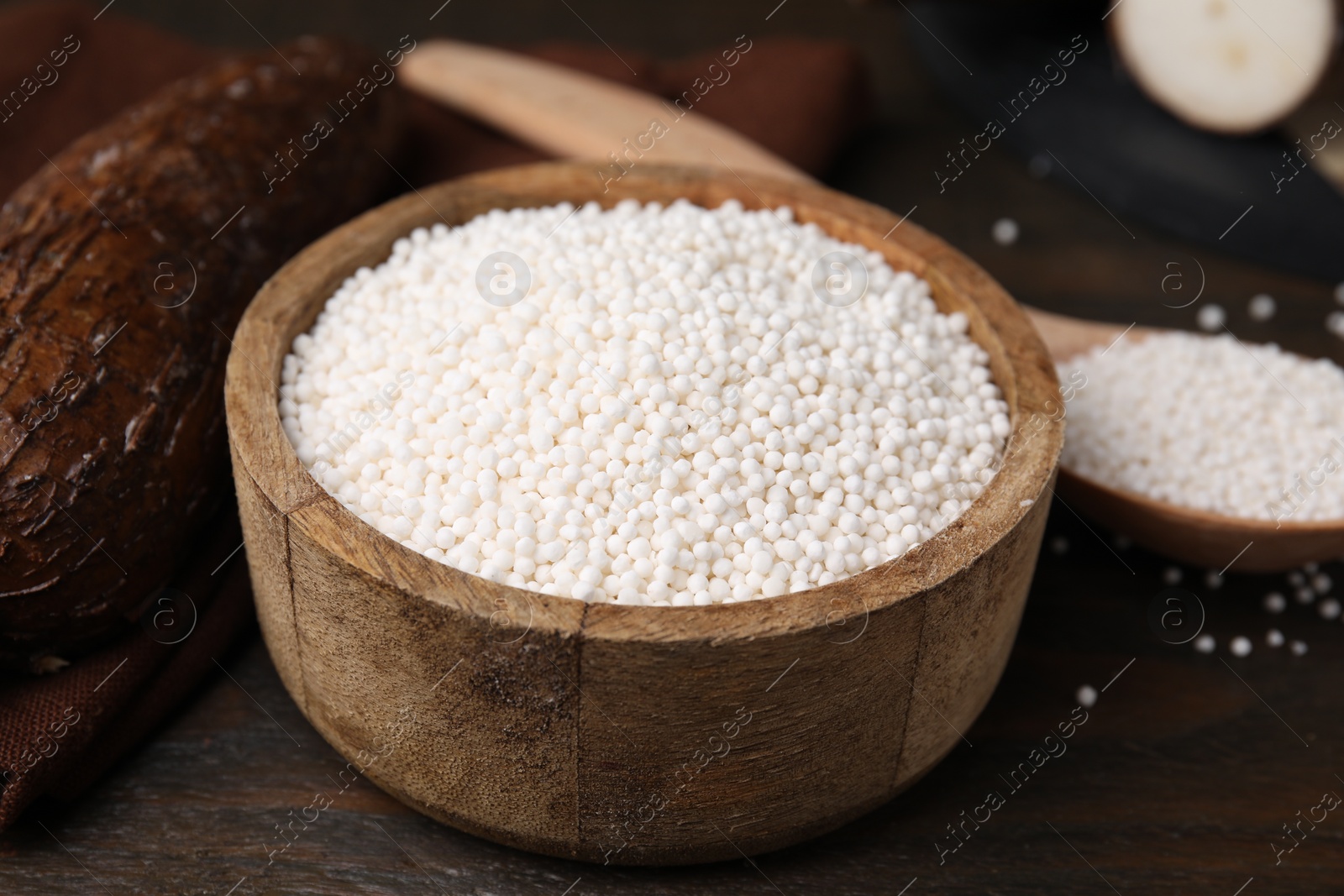 Photo of Tapioca pearls in bowl and cassava roots on wooden table, closeup