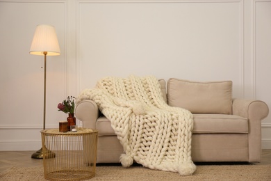 Photo of Soft knitted blanket on couch in living room. Interior element