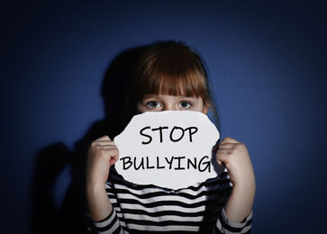 Image of Abused little girl with sign STOP BULLYING near blue wall