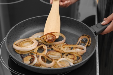 Photo of Woman cooking onion rings in frying pan on stove, closeup