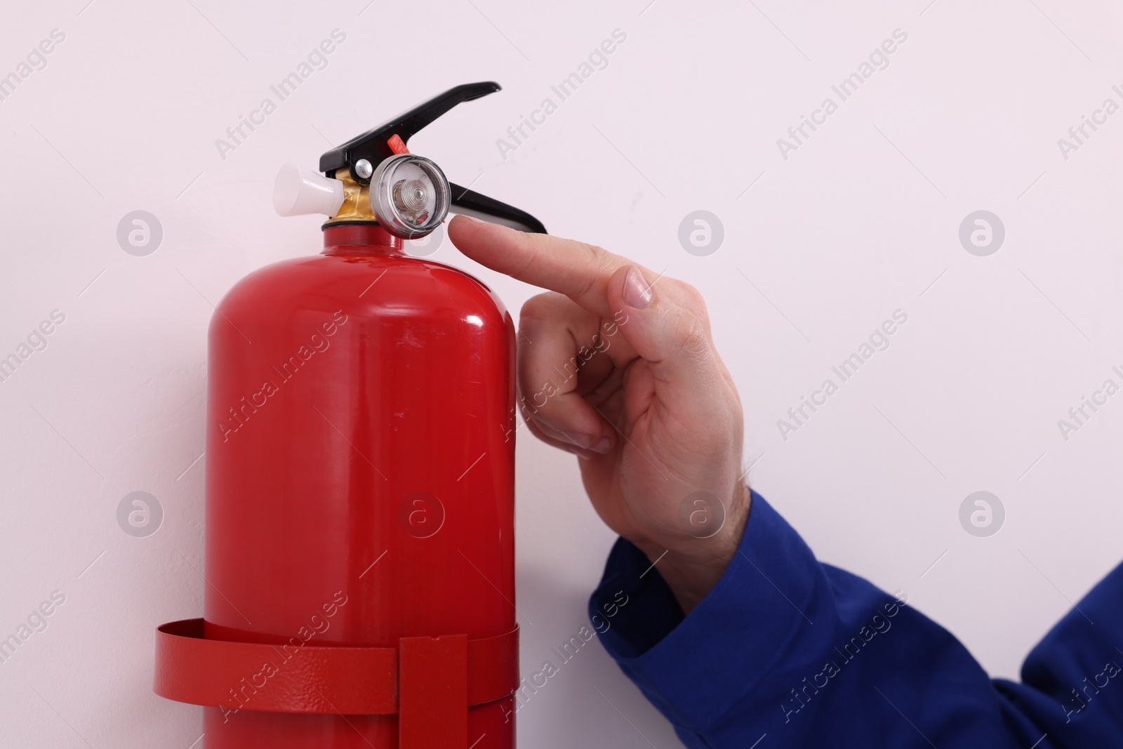 Photo of Man checking quality of fire extinguisher indoors, closeup