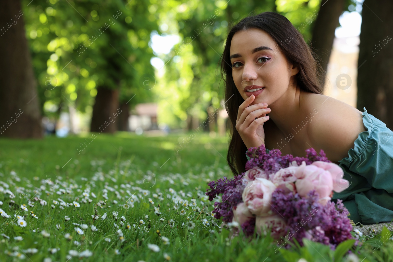 Photo of Beautiful woman with bouquet of spring flowers on green grass in park, space for text