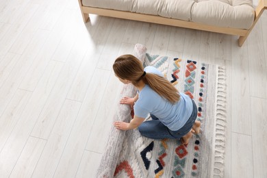 Photo of Woman unrolling carpet with beautiful pattern on floor in room, view from above. Space for text